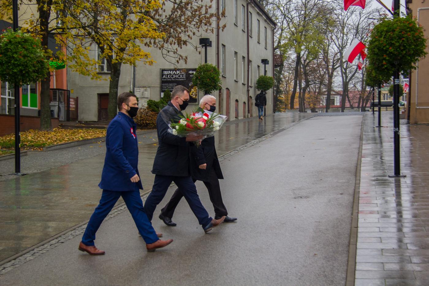Zdjęcie przedstawia Roberta Burchana Przewodniczącego Rady Miejskiej, Waldemara Sikorę Burmistrza Miasta i Gminy Busko-Zdrój, Michała Marońskiego Z-cę Burmistrza Miasta i Gminy Busko-Zdrój składających wiązankę na płycie Marszałka Józefa Piłsudskiego przy Galerii Sztuki BWA ,,Zielona”. 